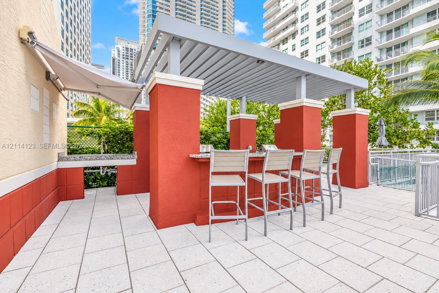 Outdoor kitchen area featuring a built-in stone-surface counter, integrated grill, overhead louvered pergola, and tiled patio flooring