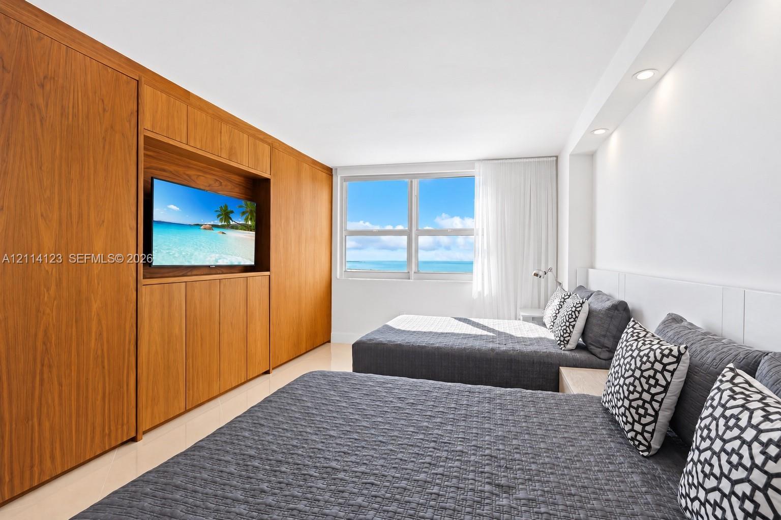Custom wood-veneer cabinetry with integrated media shelving, large windows with water scenery, and recessed lighting