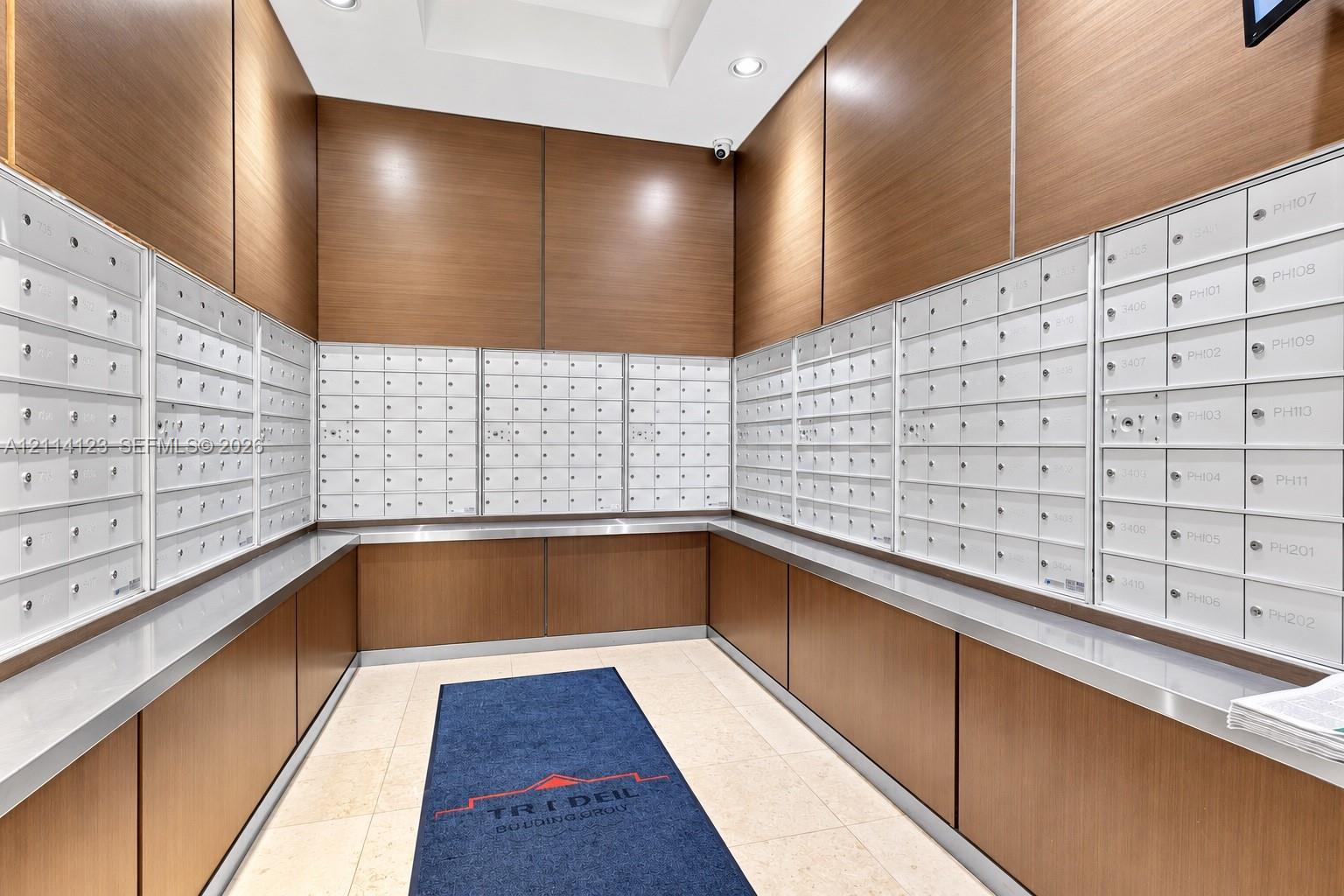 Mail center featuring floor-to-ceiling wood-finish paneling, white metal parcel boxes, recessed lighting, and stone flooring