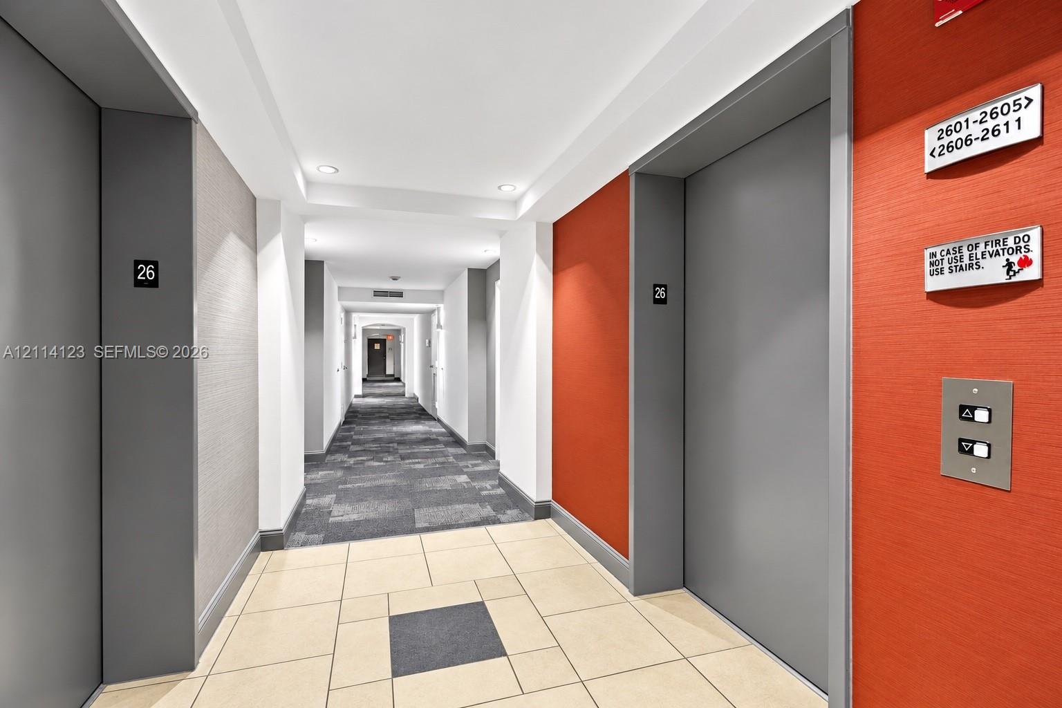 Elevator lobby featuring metallic-finish doors, textured wall treatments, integrated recessed lighting, and large-format ceramic tile flooring