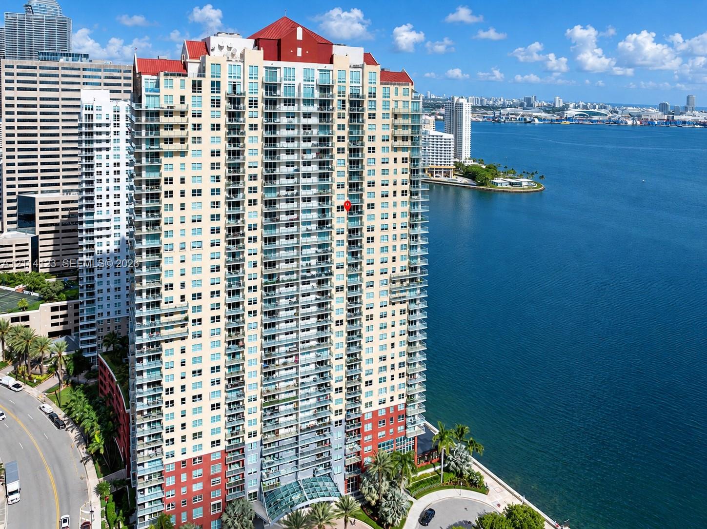 High-rise residential tower featuring a glass facade, multiple levels of private balconies, a distinctive red peaked roof, and direct waterfront placement