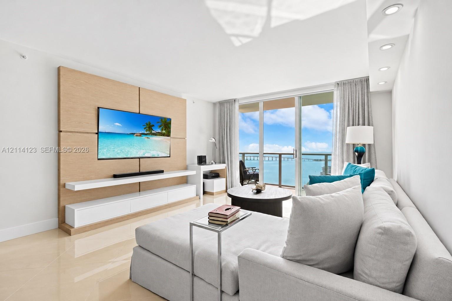Living area featuring floor-to-ceiling glass sliding doors, custom wood-paneled accent wall with built-in cabinetry, polished stone flooring, and recessed ceiling lighting