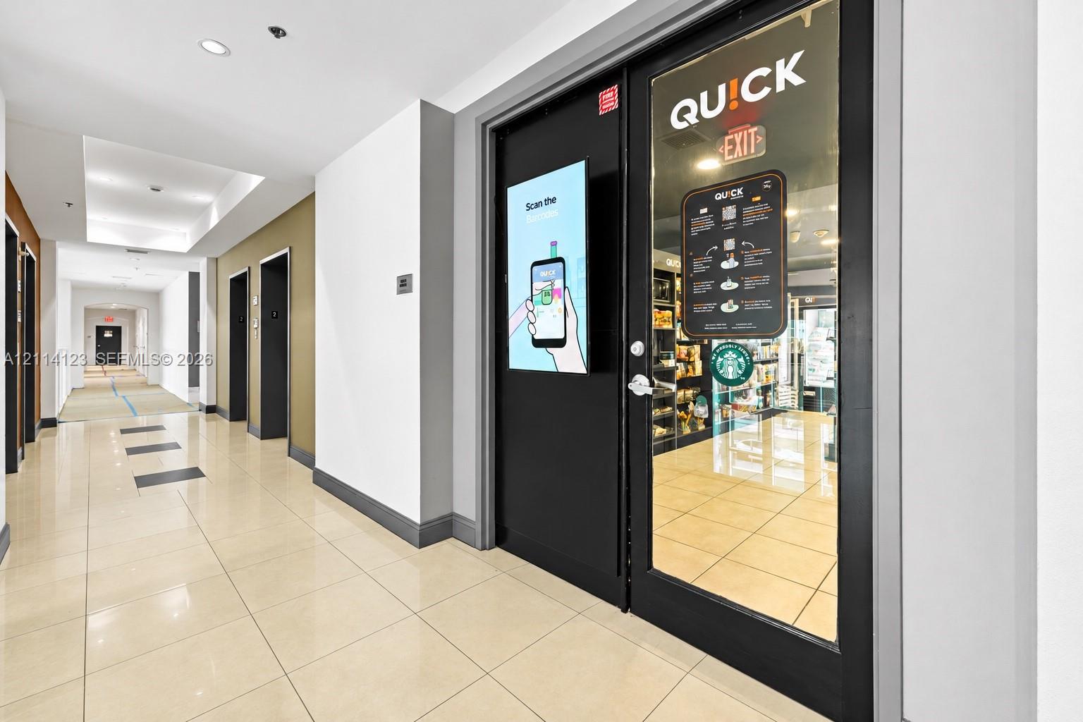 Common area hallway featuring polished tile flooring, recessed ceiling lighting, and a glass-paneled entry door with integrated digital signage