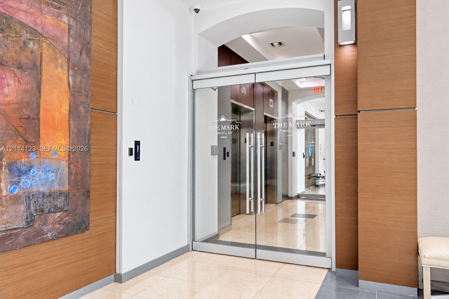 Entrance featuring glass double doors, polished stone flooring, wood-panel wall accents, and recessed wall-mounted sconces