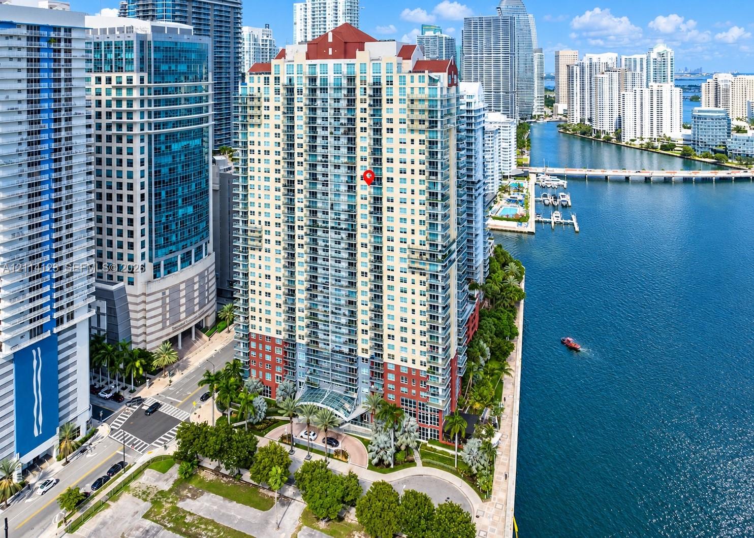 High-rise residential tower featuring a tiered facade, multi-level balconies, expansive glass windows, and a prominent red pitched roof, situated along the waterfront