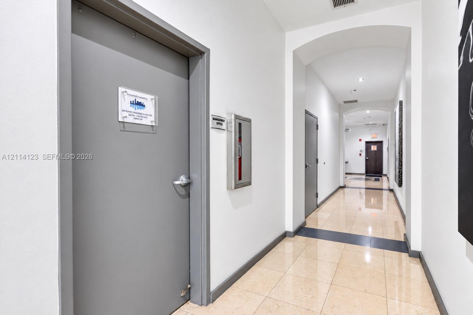 Interior hallway featuring polished tile flooring, recessed lighting, arched architectural details, and a flush-mounted metal fire extinguisher cabinet