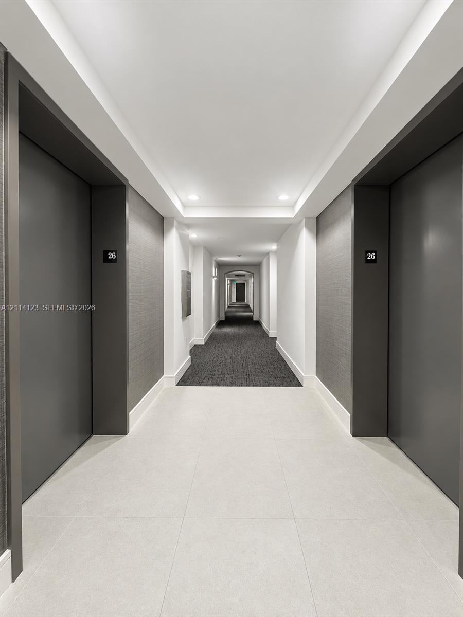 Hallway featuring large-format tile flooring, textured charcoal wall coverings, matte charcoal door frames, and recessed ceiling lighting