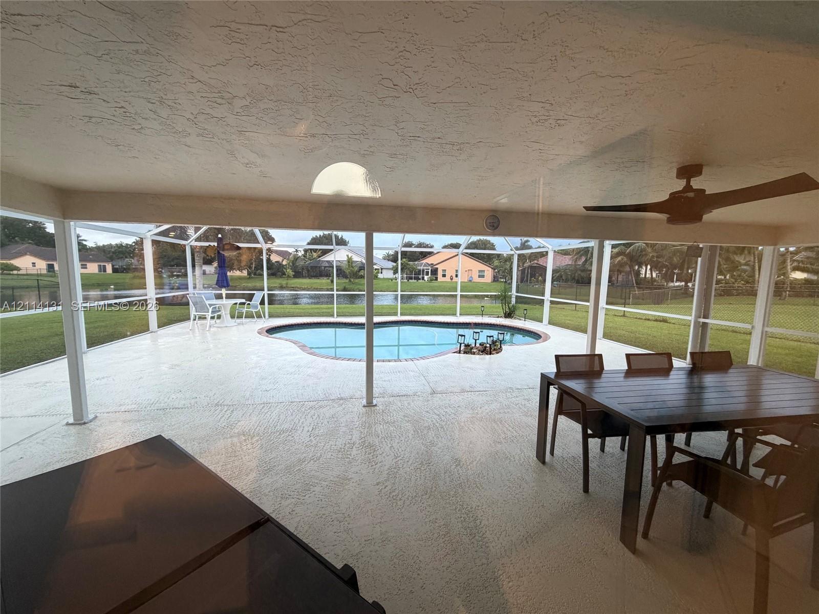 Screened-in lanai featuring a concrete patio, built-in ceiling fan, and kidney-shaped pool overlooking the water