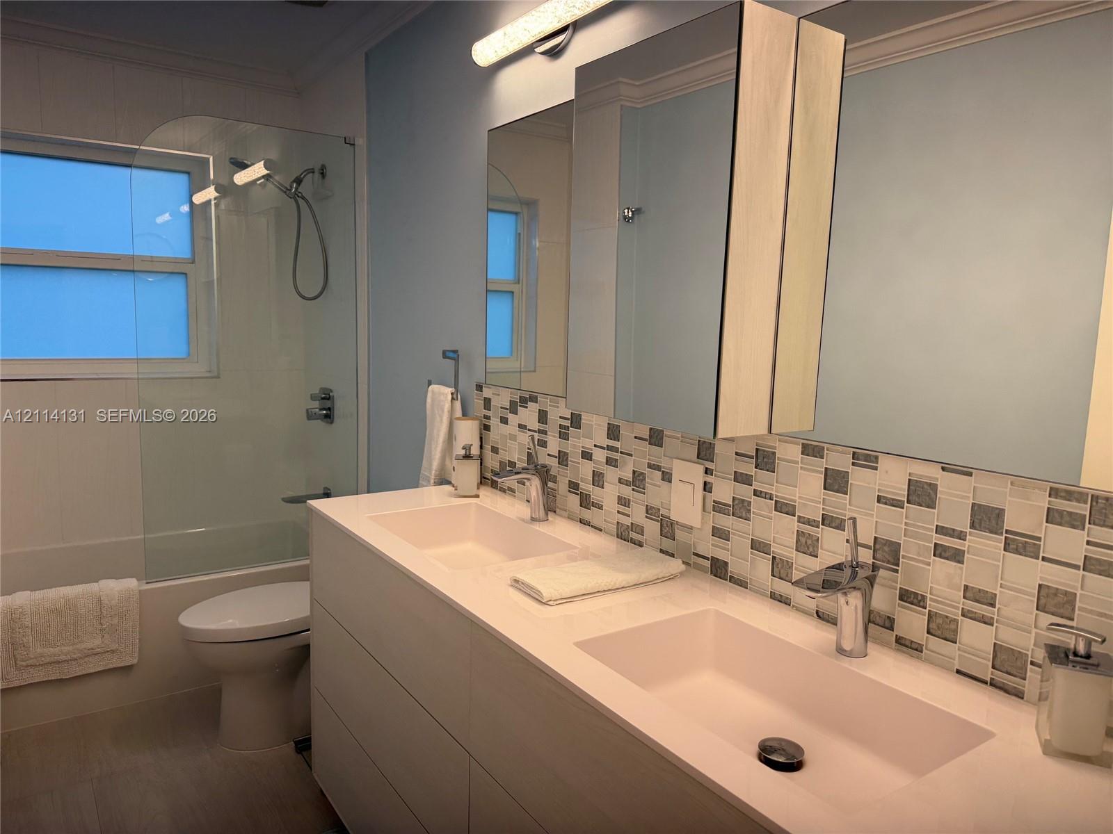 Double vanity with an integrated countertop, rectangular vessel sinks, chrome fixtures, mosaic tile backsplash, and wall-mounted medicine cabinets
