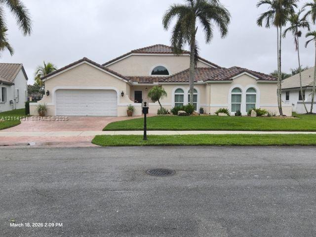 Stucco exterior residence featuring a tile roof, arched windows, an attached two-car garage, and landscaped front lawn Stucco exterior residence featuring a tile roof, arched windows, an attached two-car garage, and landscaped front lawn