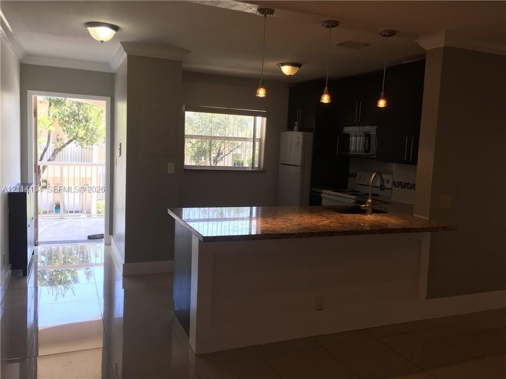 Kitchen featuring a breakfast bar, dark-finish cabinetry, tile flooring, pendant lighting, and a doorway providing access to a balcony