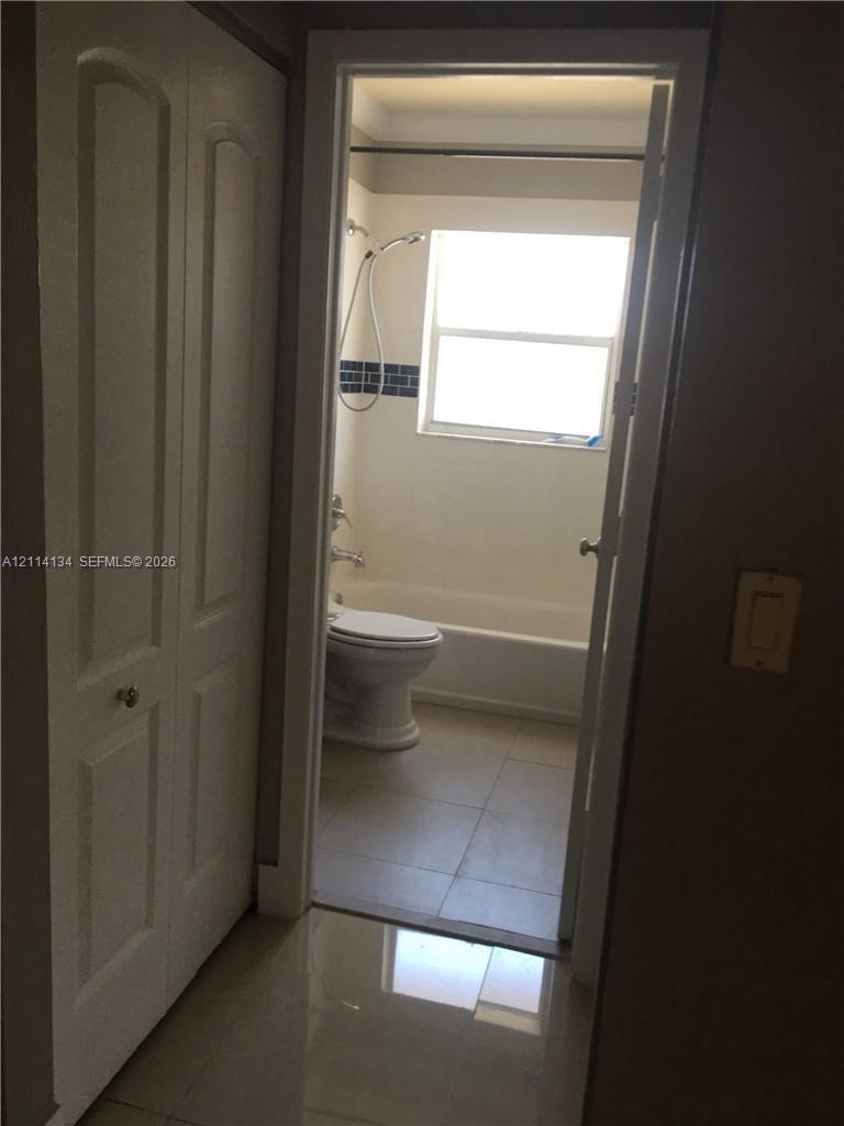 Bathroom featuring a combination bathtub and shower, porcelain tile flooring, and a window for natural light