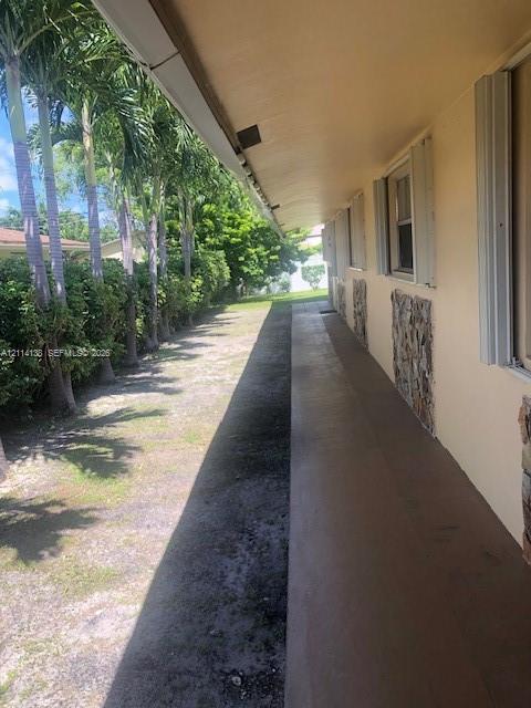 Covered concrete exterior walkway featuring vertical stone masonry accents and aluminum window shutters