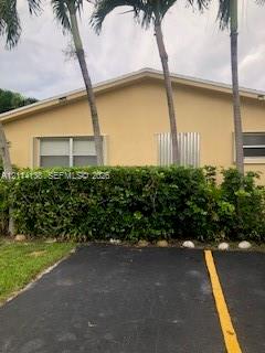 Stucco exterior featuring a gabled roofline, mature palm trees, and landscaped hedging, set alongside an asphalt parking surface Stucco exterior featuring a gabled roofline, mature palm trees, and landscaped hedging, set alongside an asphalt parking surface