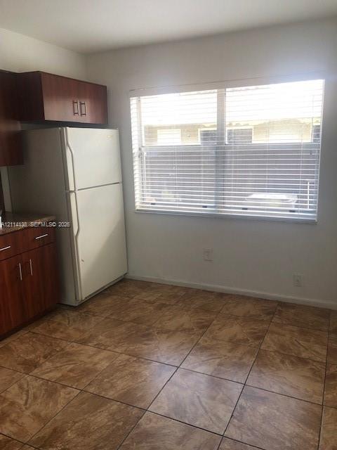 Kitchen featuring wood-finish cabinetry, stone-texture laminate countertops, large-format tile flooring, and a window with horizontal blinds Kitchen featuring wood-finish cabinetry, stone-texture laminate countertops, large-format tile flooring, and a window with horizontal blinds