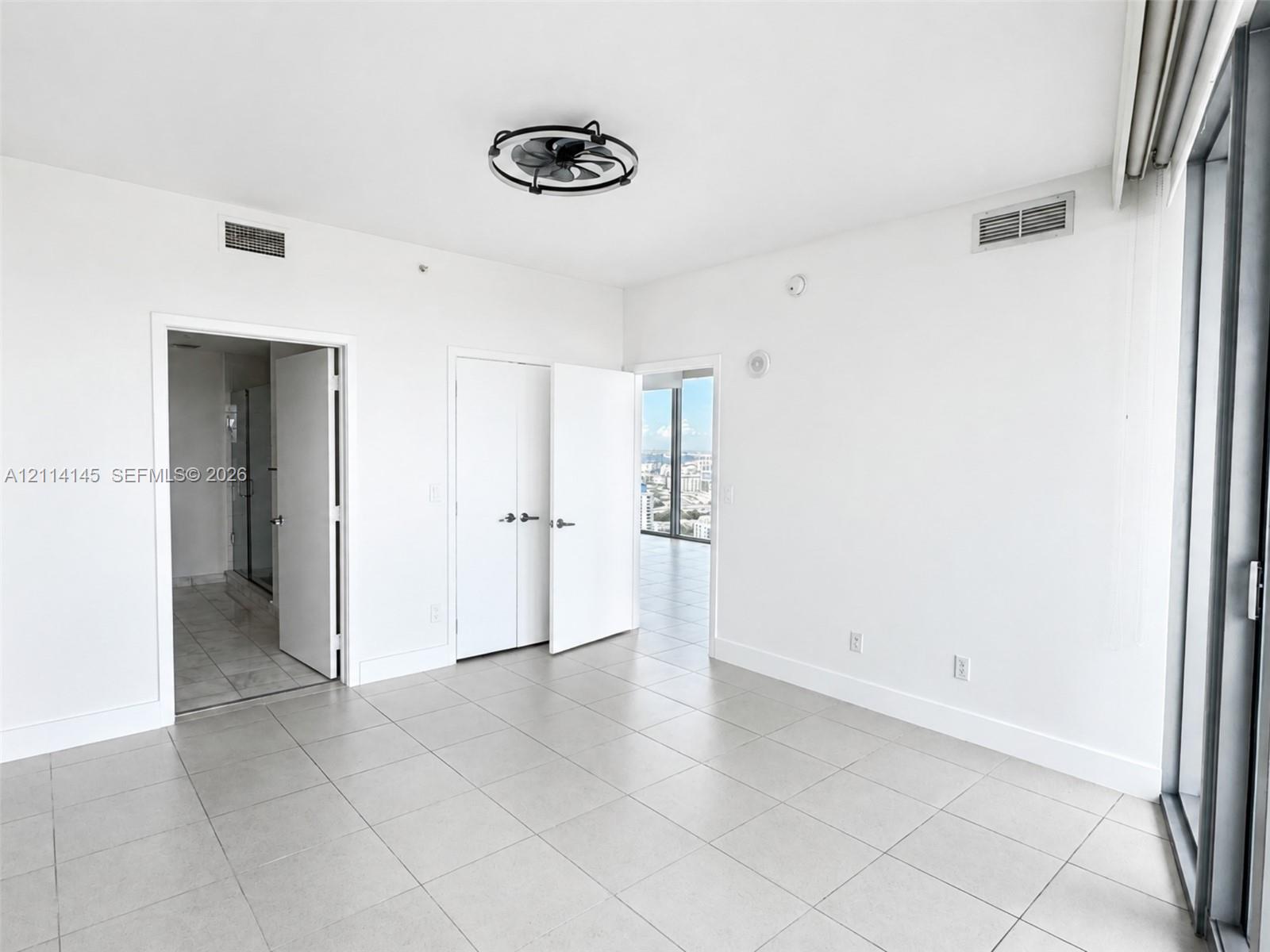 Room featuring large-format tile flooring, a minimalist industrial-style flush-mount ceiling fan, double-door closet cabinetry, and floor-to-ceiling glass paneling