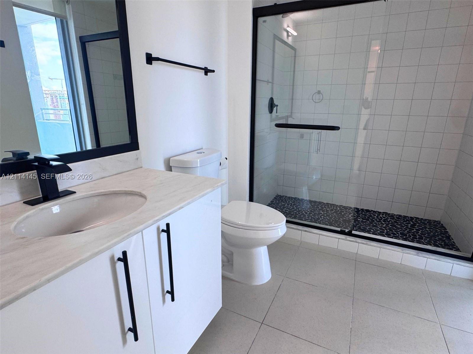 Bathroom featuring a vanity with a light-toned countertop, an integrated sink with a matte black faucet, a walk-in shower with a glass enclosure and pebble-stone flooring, and matte black hardware