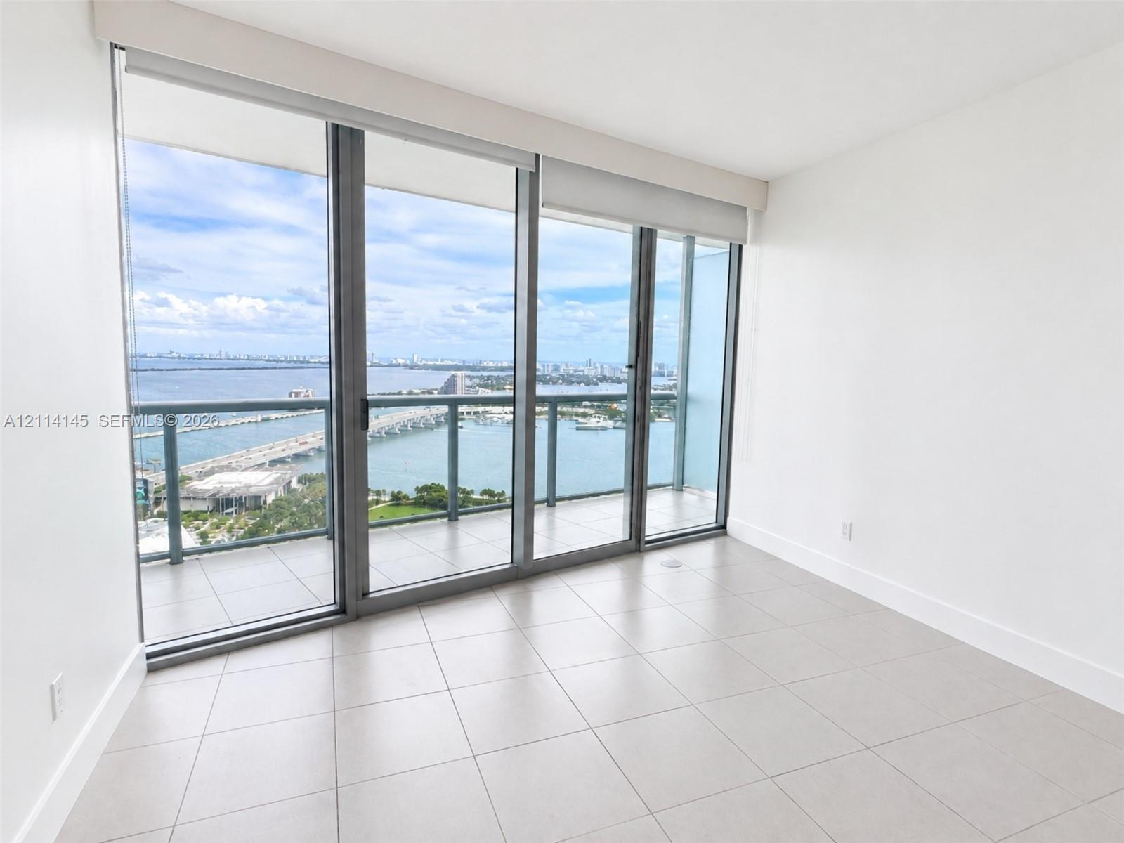 Floor-to-ceiling windows, ceramic tile flooring, and a glass-paneled balcony featuring expansive water and skyline scenery
