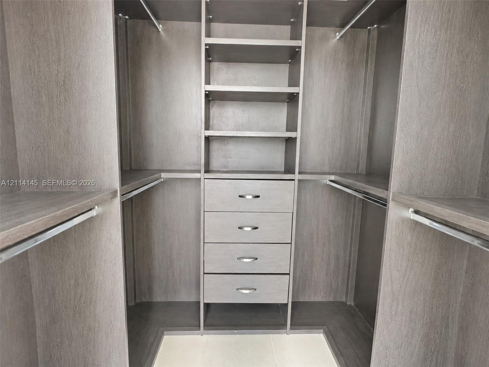 Custom closet organization system featuring wood-finish cabinetry, four integrated storage drawers with brushed metal pulls, adjustable shelving, and multiple hanging rods