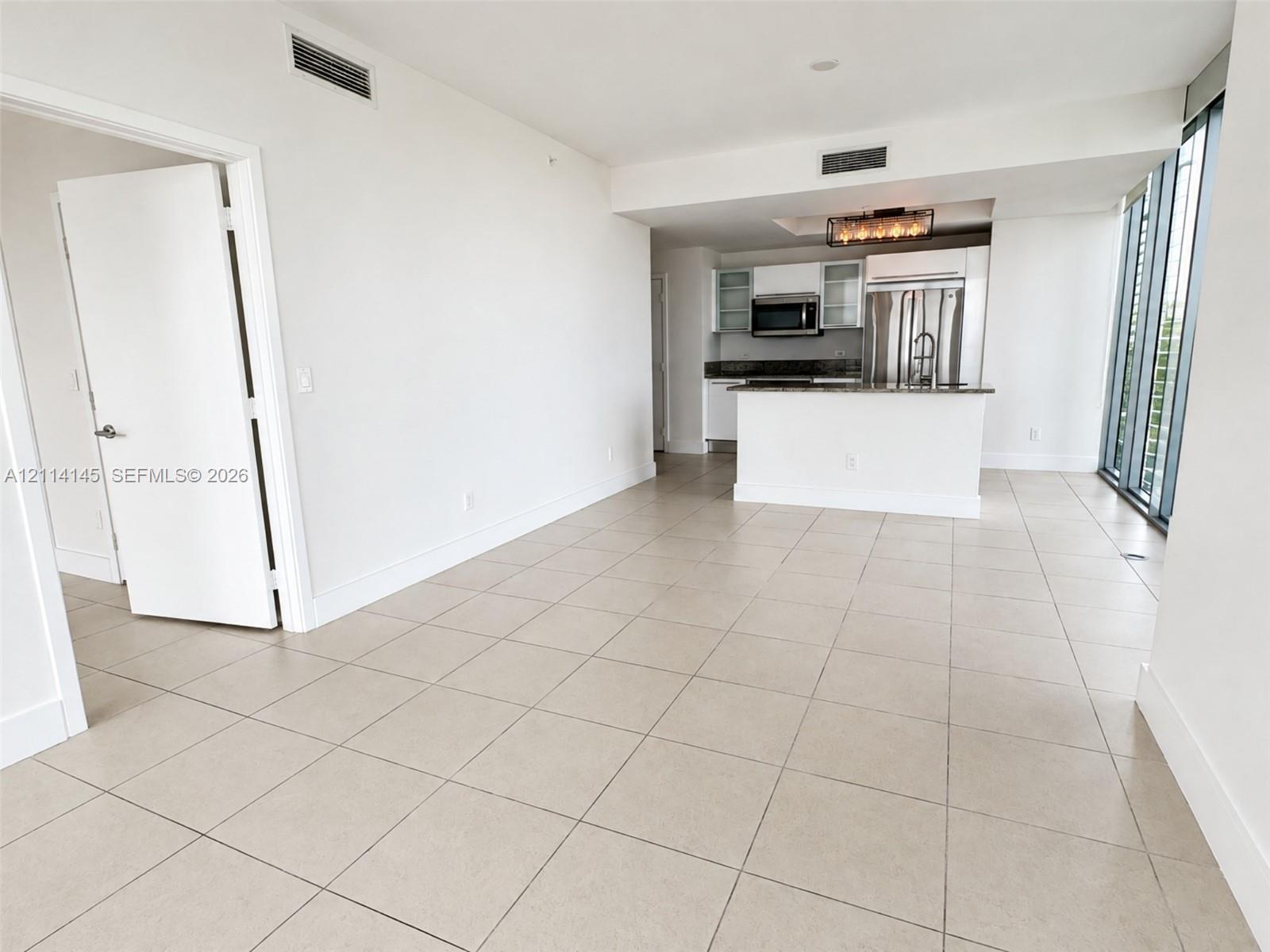 Open-concept area with tile flooring, kitchen featuring stainless steel appliances, stone-surface counters, and floor-to-ceiling windows