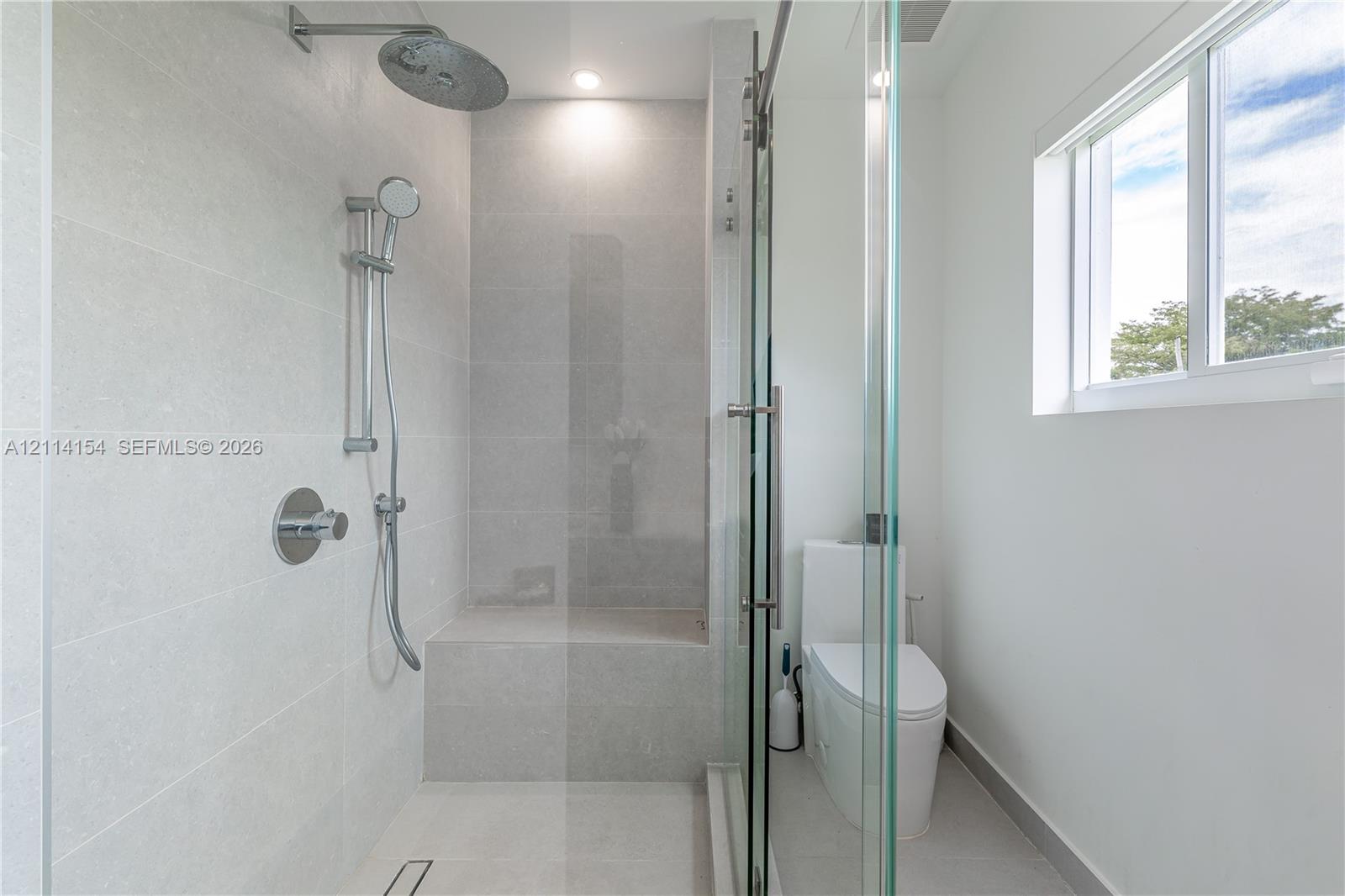 Walk-in shower with light-toned tiled surround, built-in tiled bench, rainfall shower head, adjustable handheld sprayer, and frameless glass enclosure