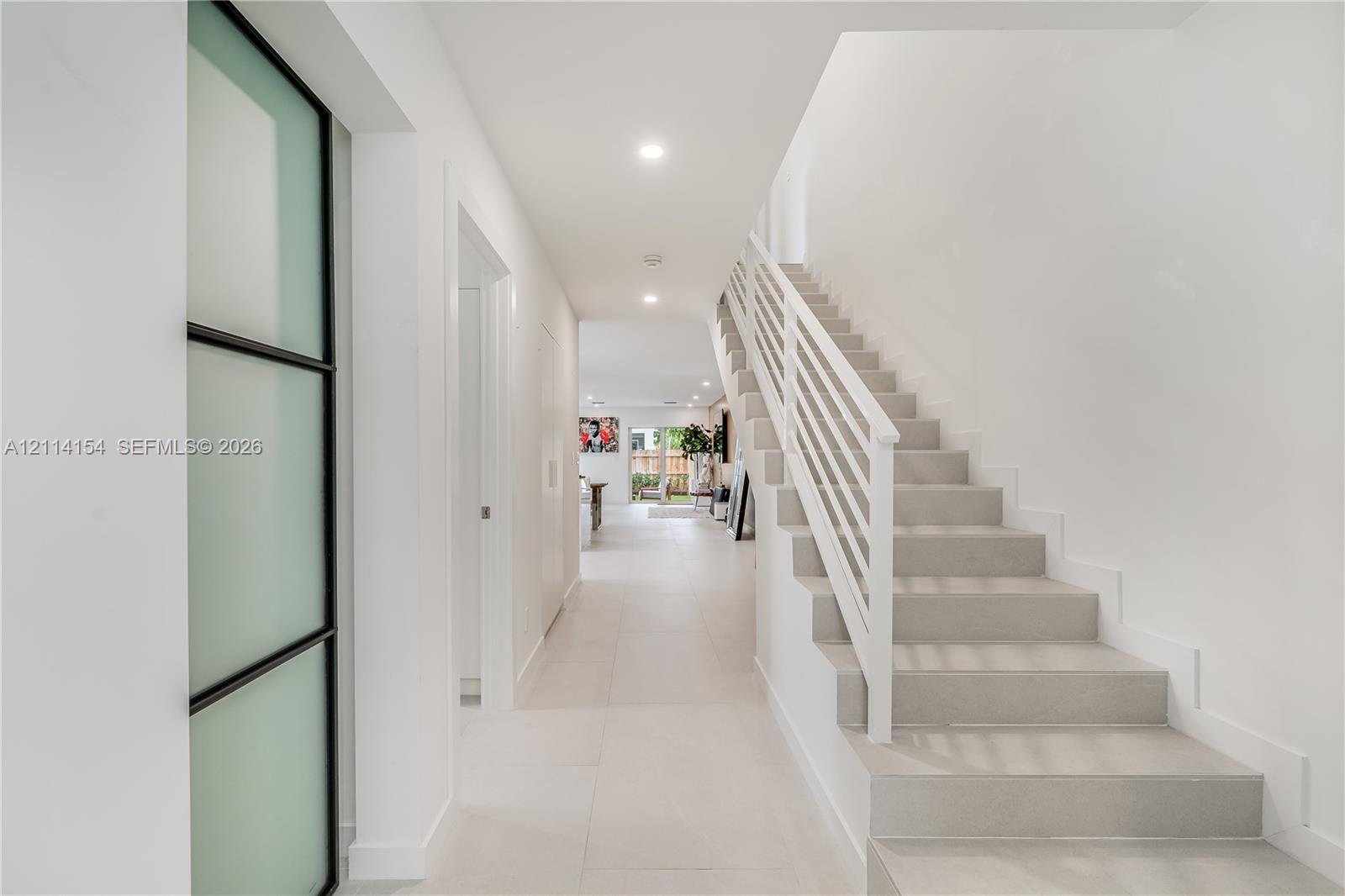 Entryway featuring large-format tile flooring, a staircase with white horizontal railings, recessed lighting, and a frosted glass door with a black frame