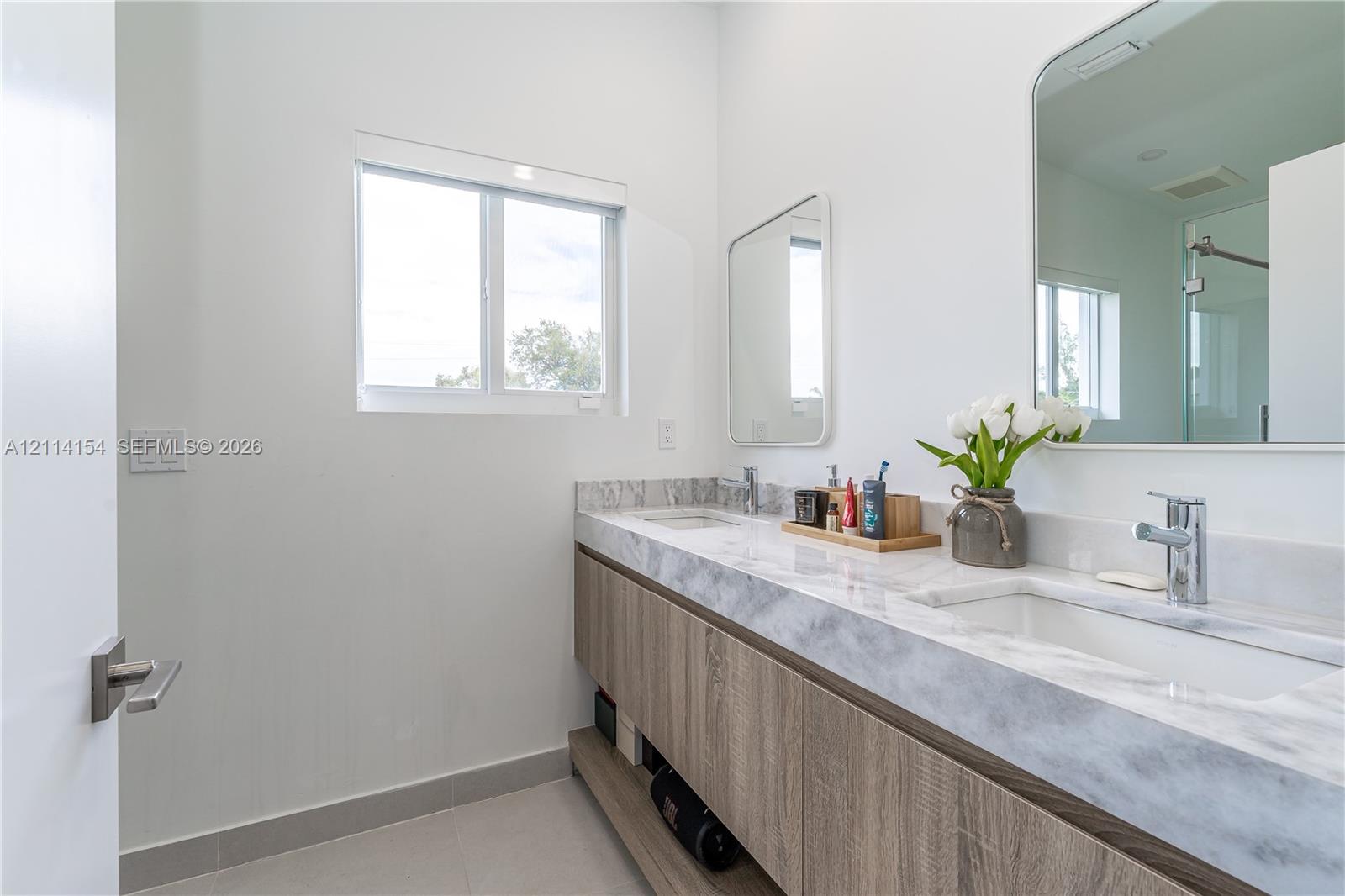 Dual-sink floating vanity with wood-finish cabinetry, stone-style countertop, rectangular undermount sinks, and rounded rectangular mirrors