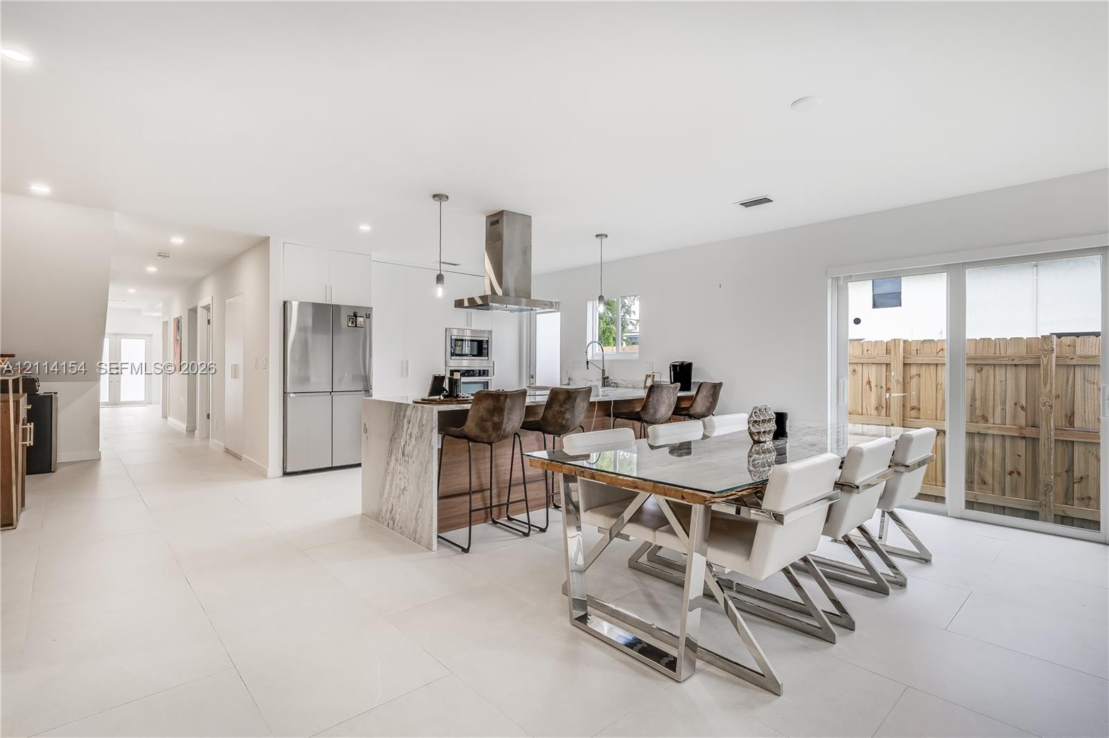 Kitchen featuring a waterfall-edge island, stone-patterned countertop, stainless steel appliances, stainless steel range hood, and large-format tile flooring