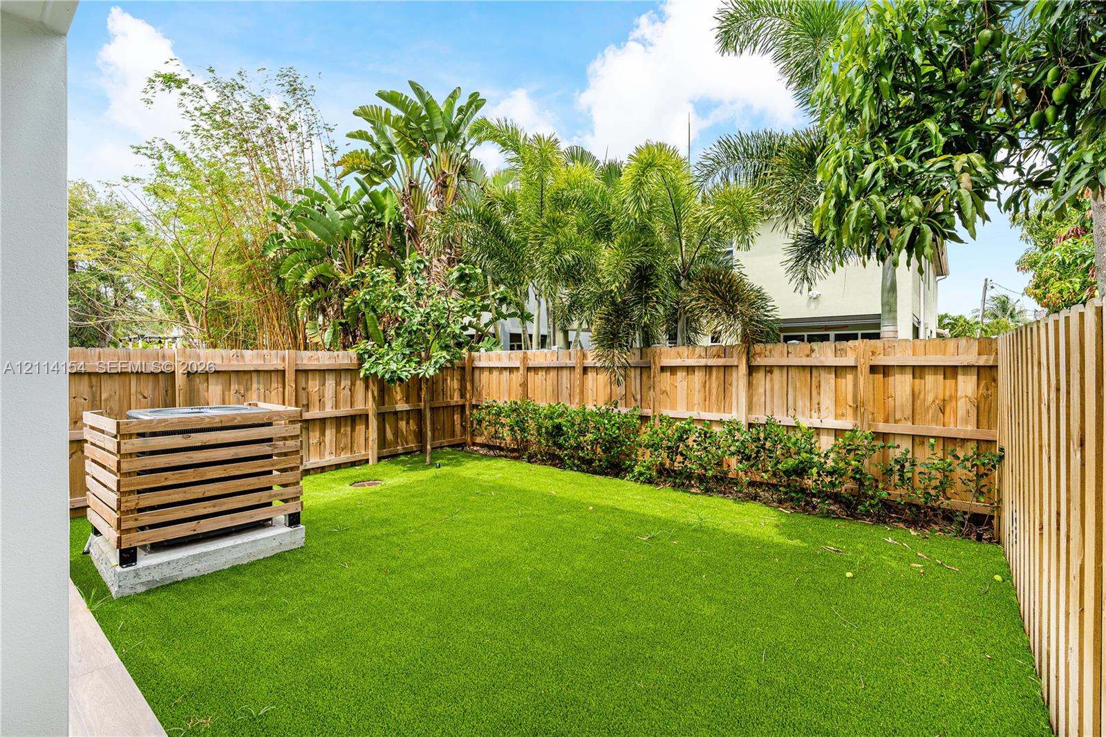 Private backyard featuring synthetic turf, vertical wood privacy fencing, and a built-in wood slat HVAC enclosure