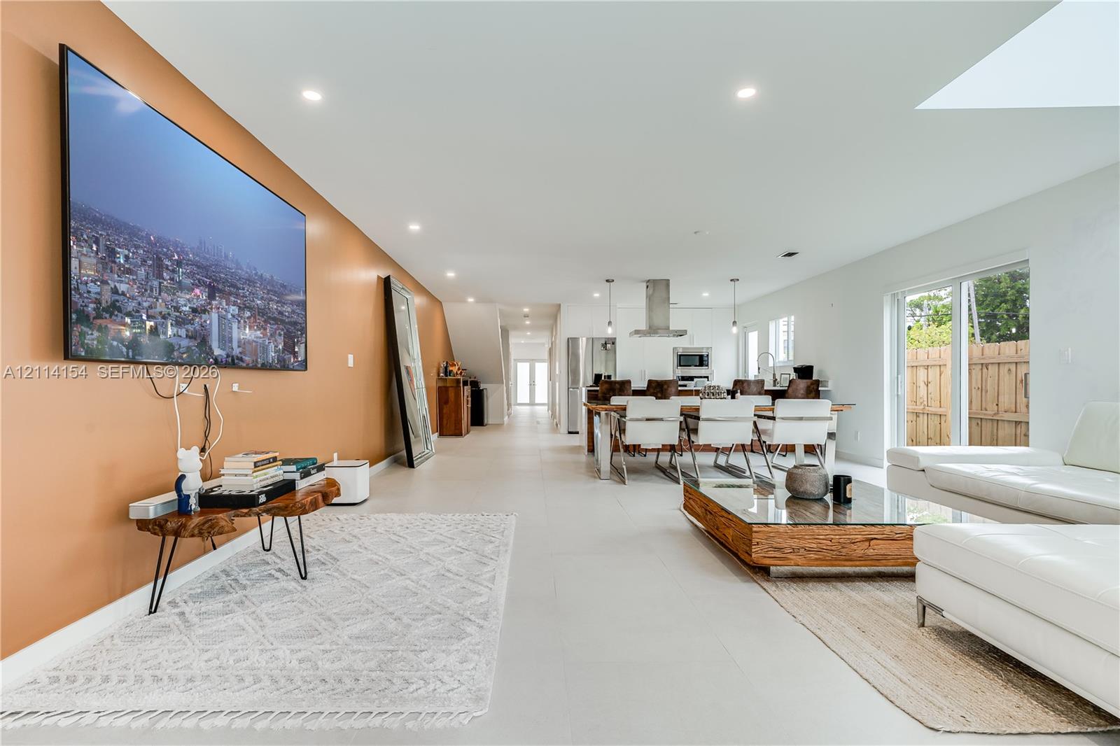 Open-concept interior featuring large-format tile flooring, recessed lighting, a stainless steel kitchen range hood, and sliding glass doors