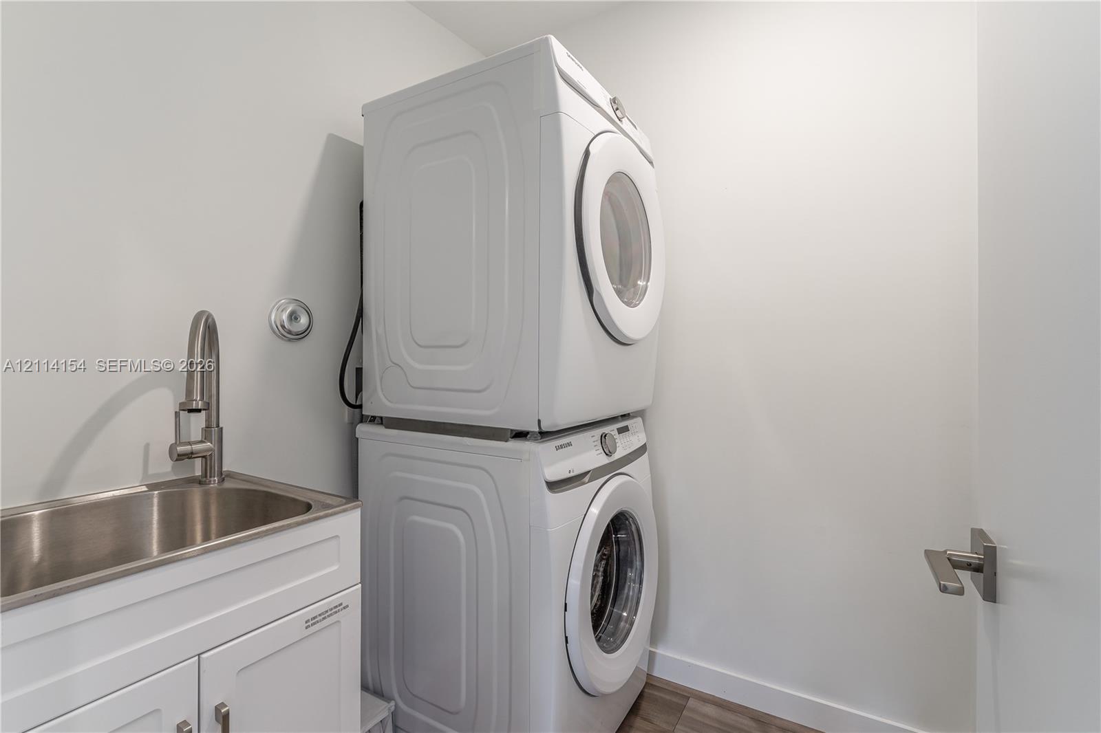 Stacked front-load laundry units with a white finish, stainless steel basin sink, and high-arc brushed nickel faucet set within a white cabinet vanity
