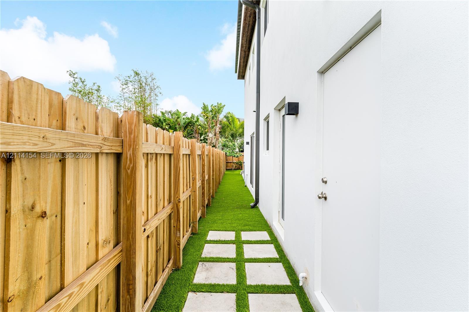 Side yard featuring a tall wood privacy fence, artificial turf, and square concrete pavers