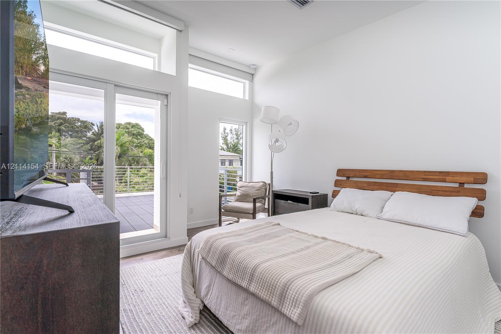 High-ceilinged room featuring expansive clerestory windows, a full-height glass door, and a private balcony with horizontal metal railings