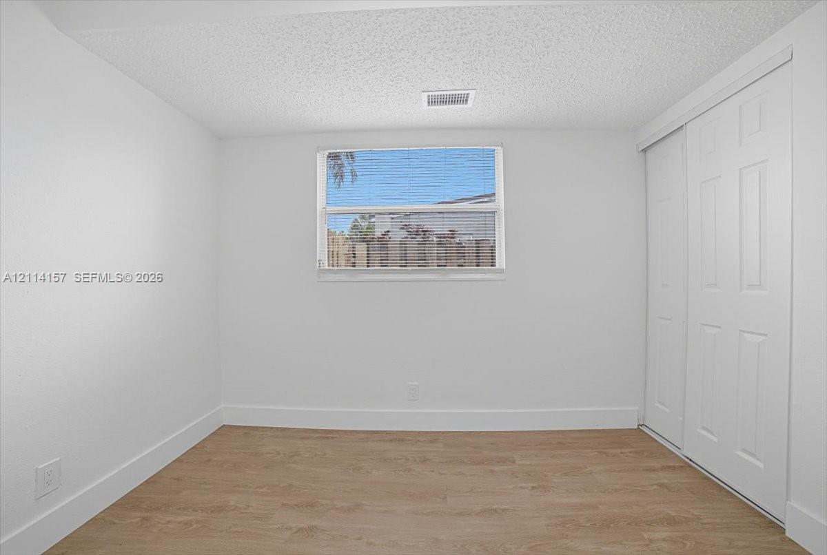 Neutral-toned room featuring wood-finish flooring, a central window with horizontal blinds, and a built-in sliding-door closet Neutral-toned room featuring wood-finish flooring, a central window with horizontal blinds, and a built-in sliding-door closet