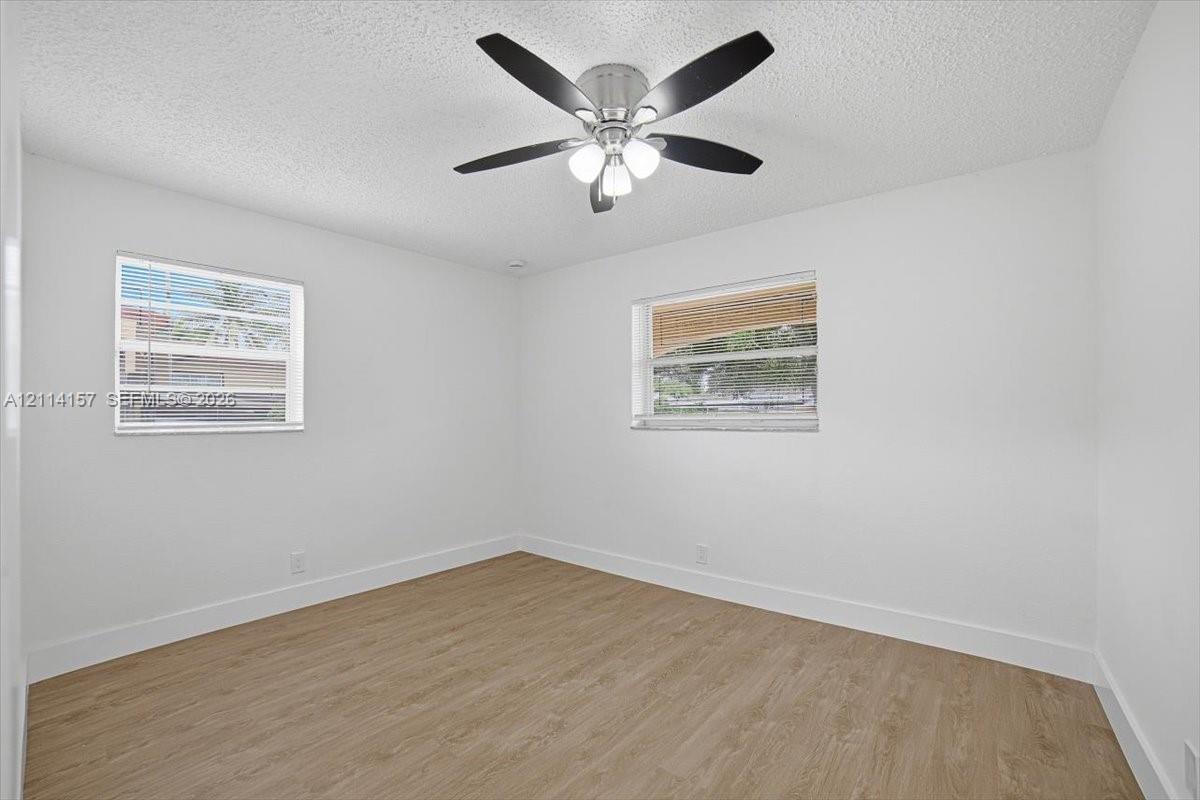 Wood-finish flooring, white walls, dual windows, and a multi-blade ceiling fan with integrated lighting