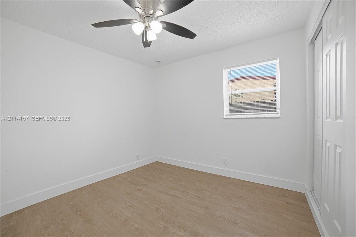 Neutral-toned wood-finish flooring, ceiling fan with integrated lighting, window with blinds, and dual-panel sliding closet doors