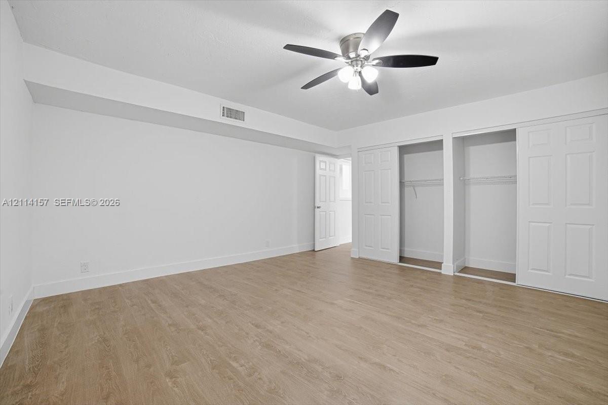 Room featuring wood-finish flooring, a multi-blade ceiling fan with integrated lighting, and dual closets with paneled sliding doors
