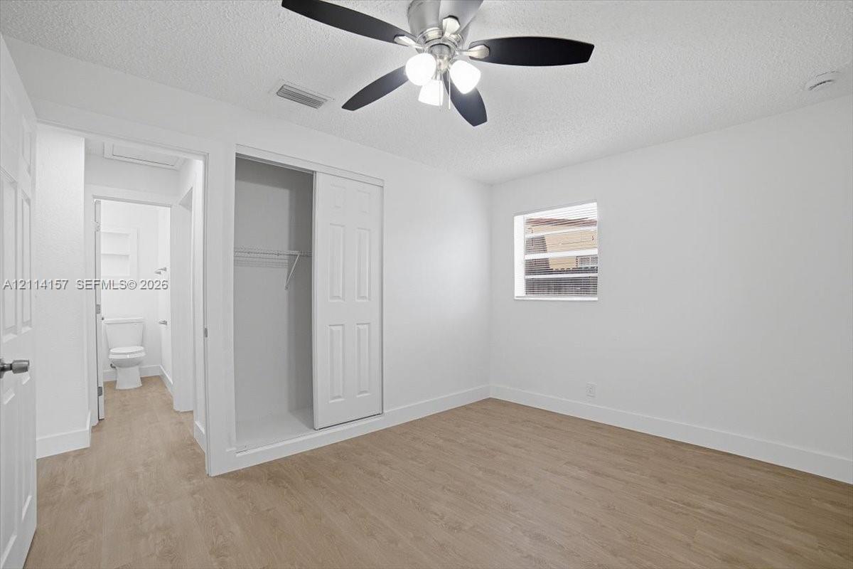 Room featuring wood-finish flooring, a ceiling fan with integrated lighting, a sliding-door closet, and white wall finishes