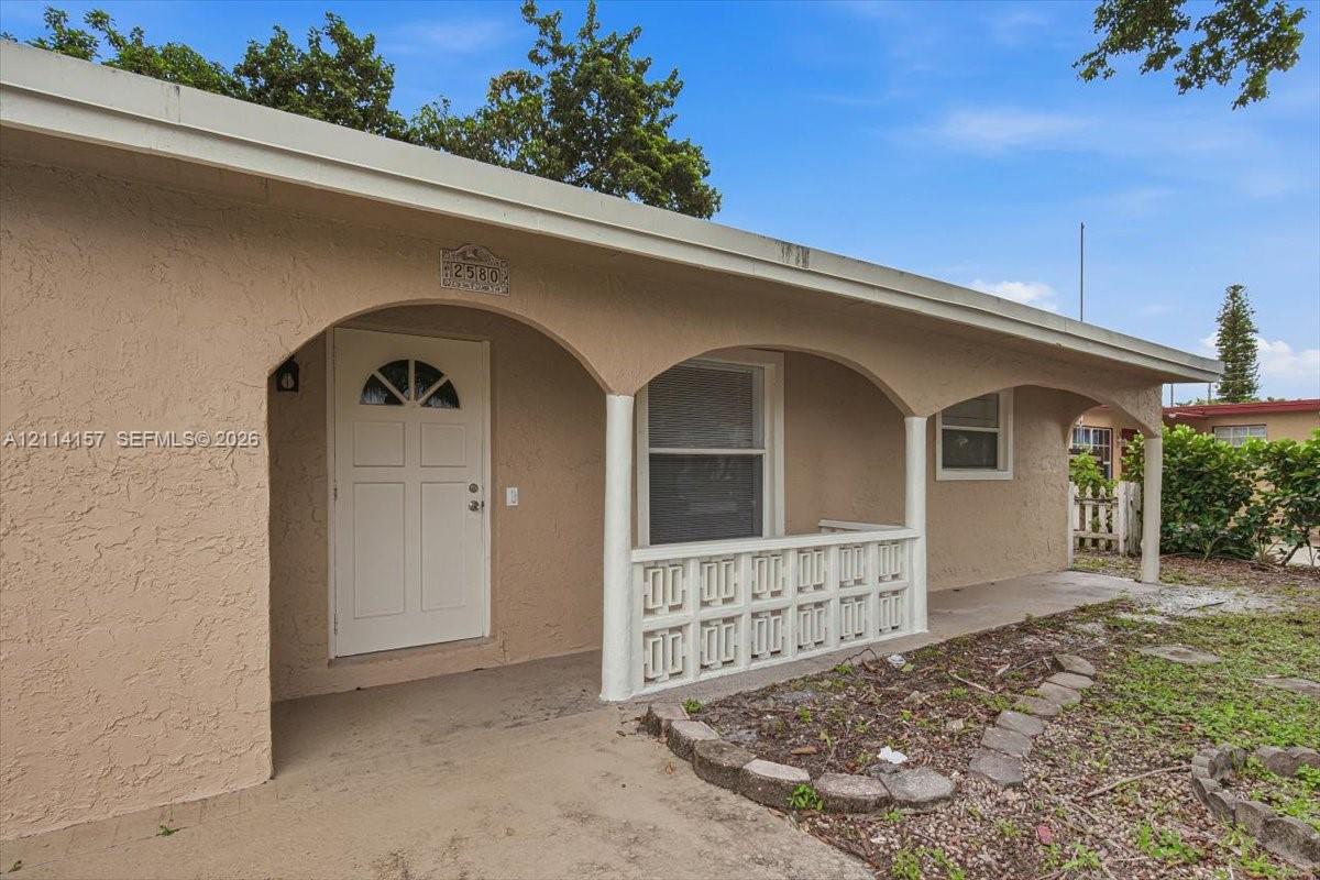 Stucco exterior featuring an arched covered porch, decorative concrete balustrade, and a solid door with arched glass inlay