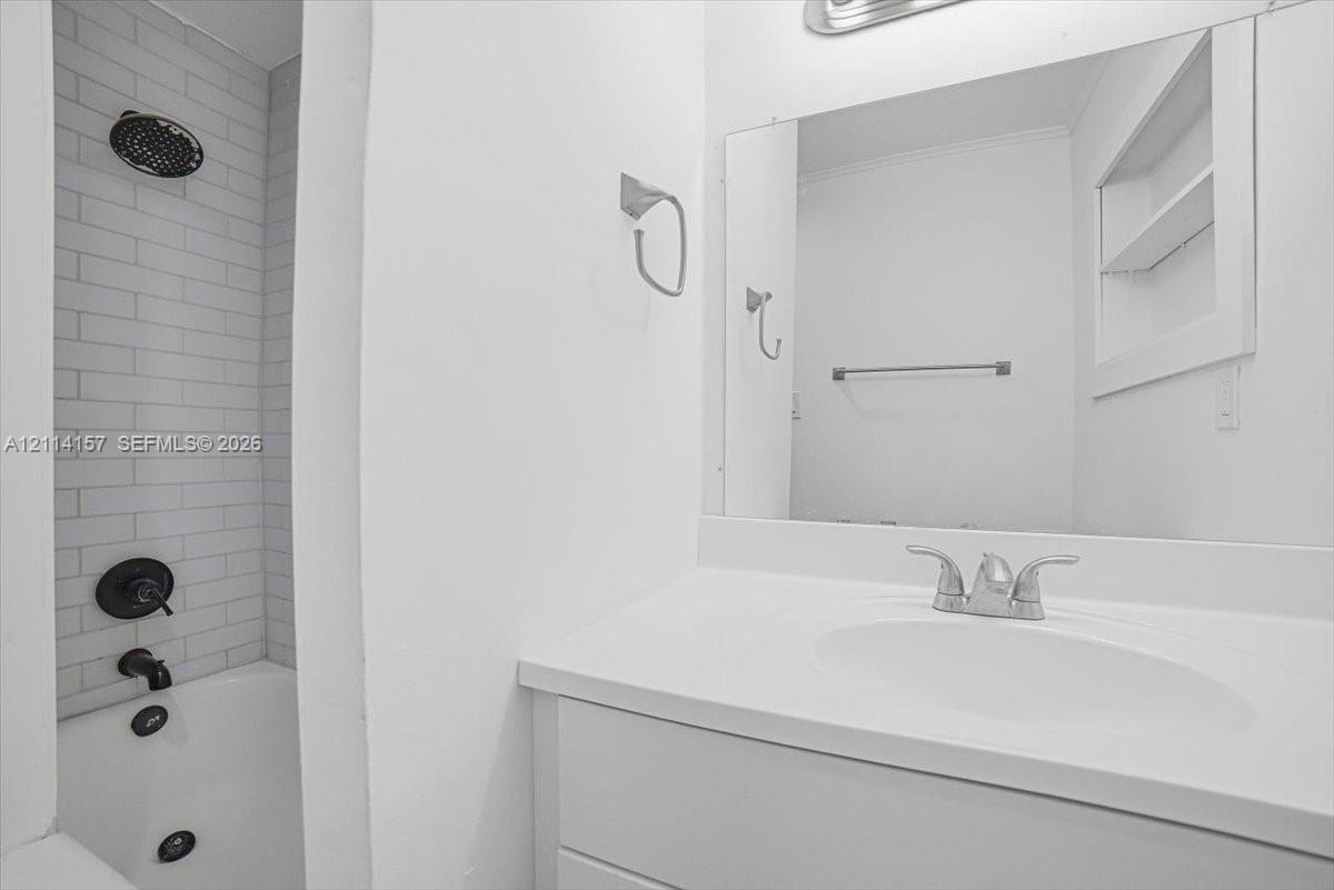 Bathroom featuring a white vanity with a composite countertop, subway tile shower surround, matte black shower fixtures, large rectangular vanity mirror, and built-in recessed shelving
