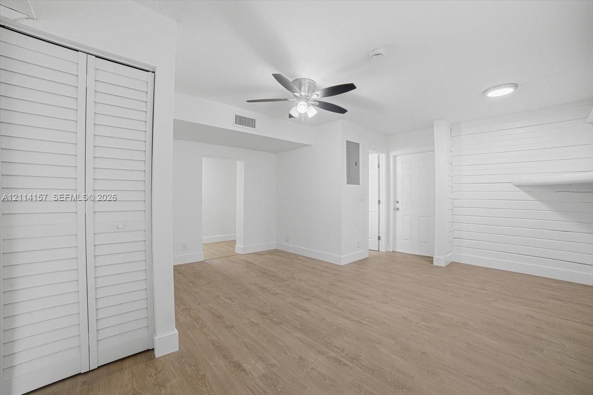 Interior space featuring wood-finish flooring, white shiplap accent wall, louvered bi-fold closet doors, and a ceiling fan with integrated lighting
