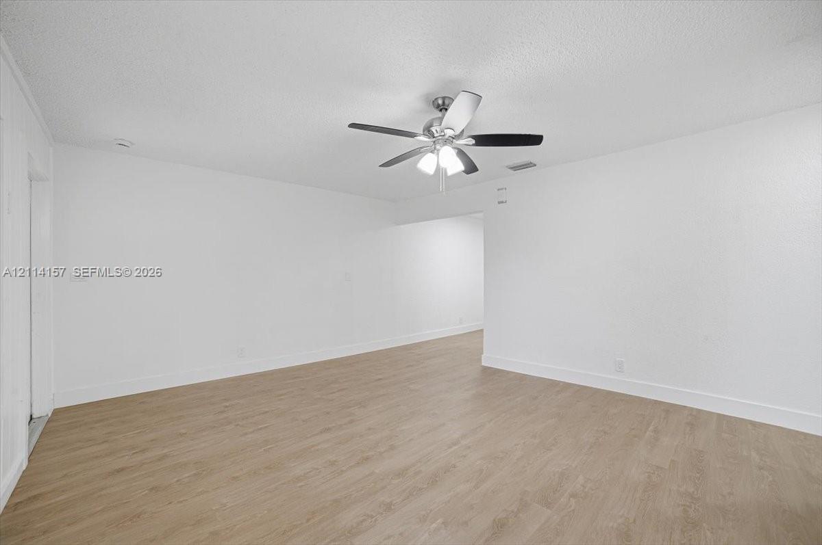 Interior space featuring wood-finish flooring, white walls, and a ceiling fan with integrated lighting