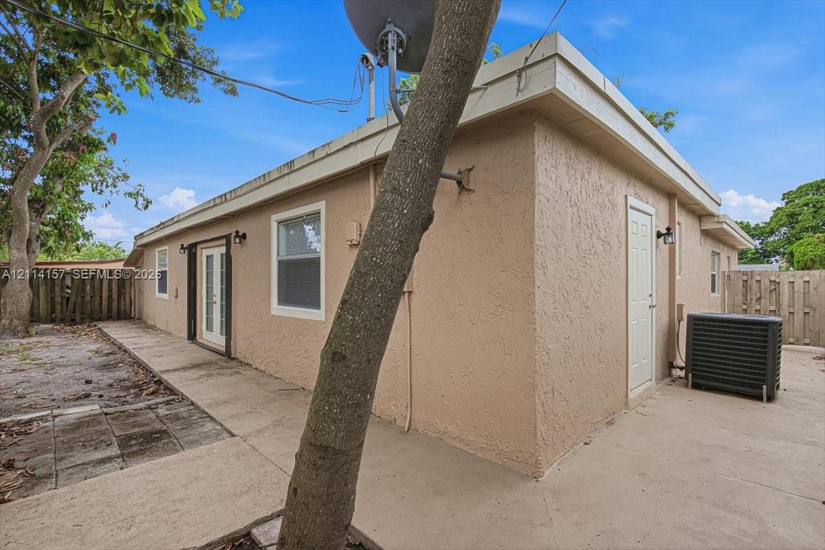 Stucco exterior featuring dual-entry doors, concrete side patio, and wood privacy fencing