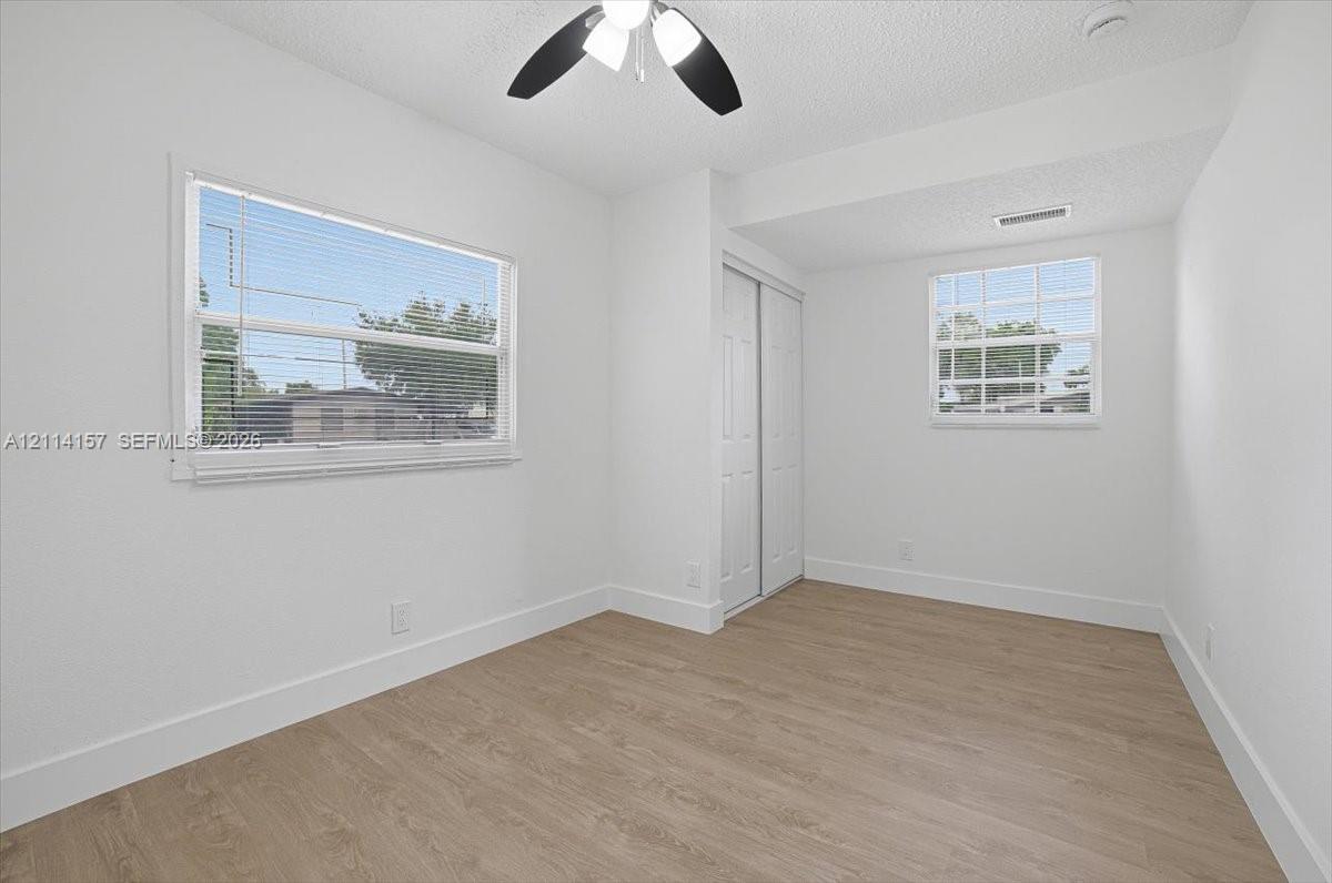 Interior room featuring wood-finish flooring, dual windows with integrated blinds, and a built-in closet with sliding panel doors Interior room featuring wood-finish flooring, dual windows with integrated blinds, and a built-in closet with sliding panel doors