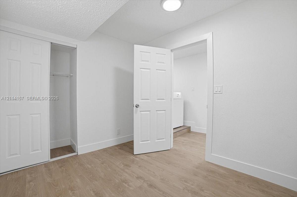 Interior space featuring wood-finish flooring, white six-panel doors, and built-in closet storage with a metal hanging rod Interior space featuring wood-finish flooring, white six-panel doors, and built-in closet storage with a metal hanging rod