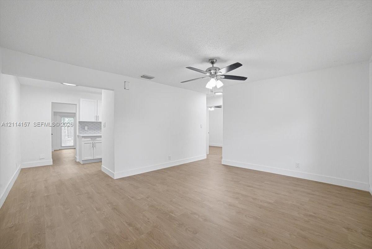 Interior space featuring wood-finish flooring, white walls, and a ceiling-mounted light fixture with a multi-blade fan