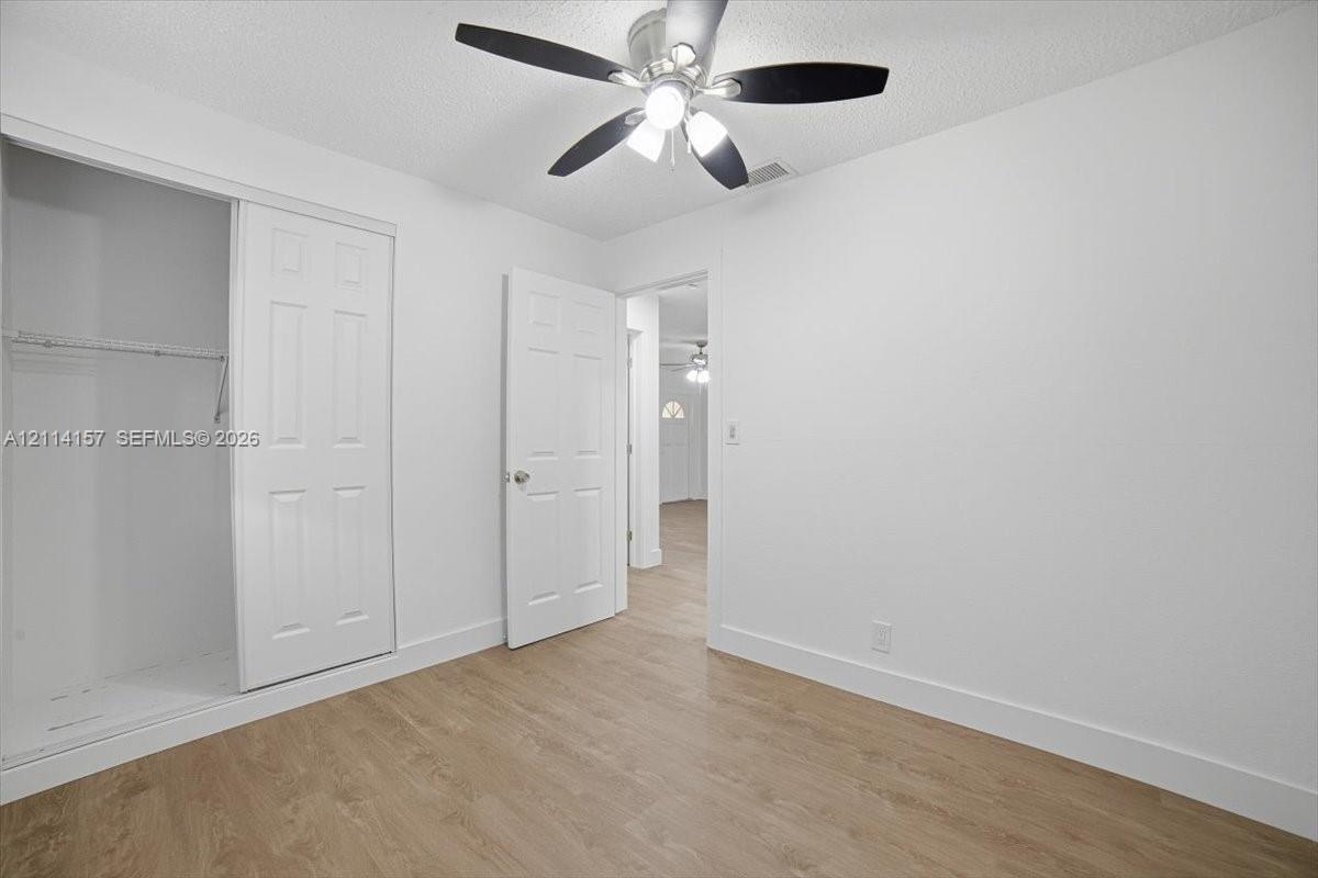 Room featuring wood-finish flooring, a ceiling fan with integrated lighting, and a closet with sliding paneled doors Room featuring wood-finish flooring, a ceiling fan with integrated lighting, and a closet with sliding paneled doors