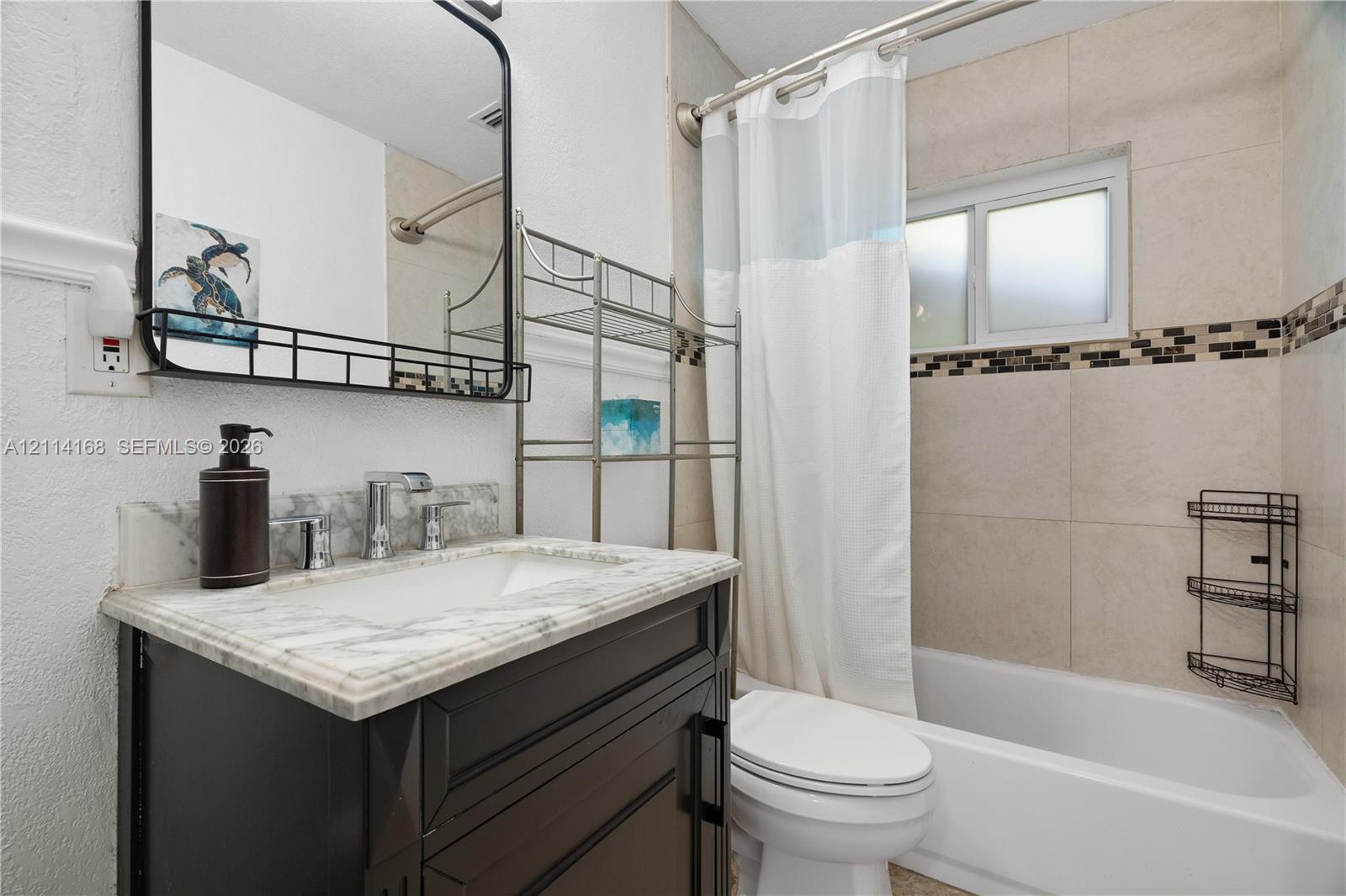 Dark wood-finish vanity with a stone-top integrated sink, rectangular framed mirror, and tiled shower surround featuring a decorative mosaic accent band
