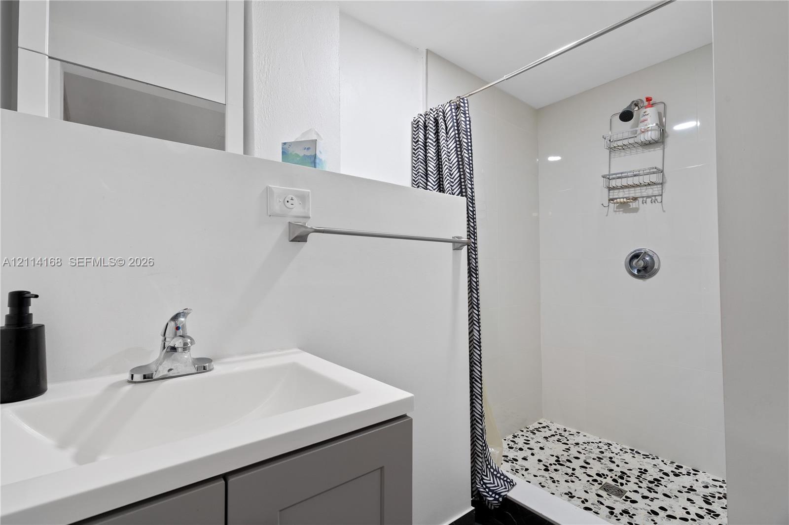 Bathroom featuring a gray vanity with a white countertop, polished chrome faucet, and a walk-in shower with white wall tile and a patterned floor (Flex space, in-law quarters)