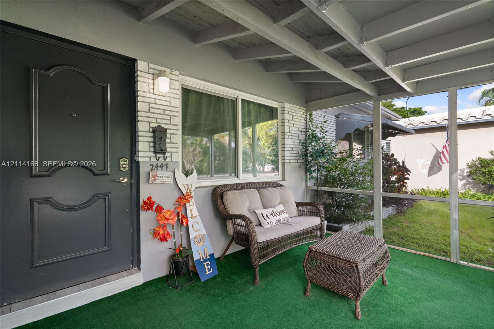 Screened-in porch featuring a painted brick facade, an exterior door with architectural paneling, and an exposed beam ceiling